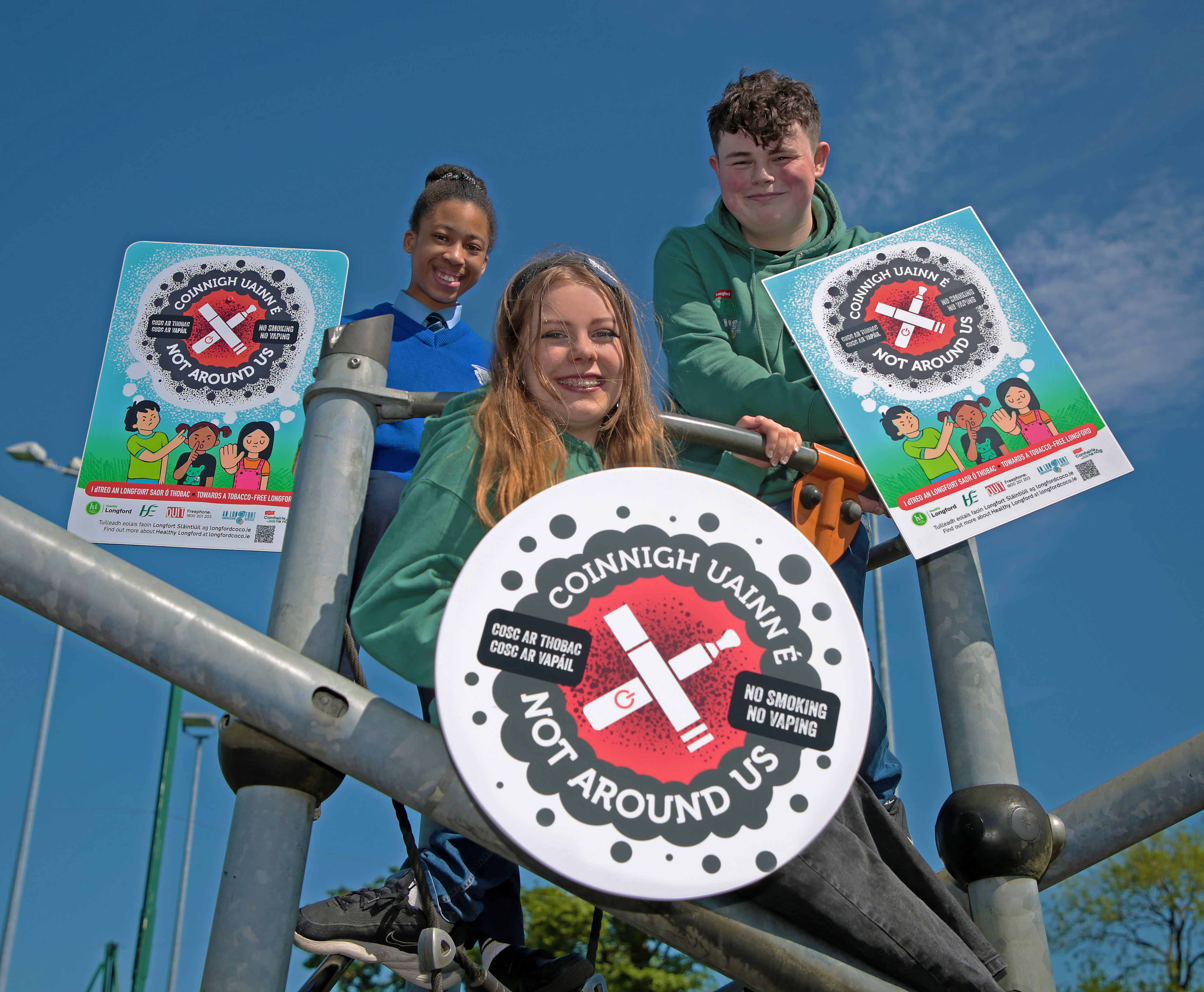 CB3B0160 Three young people on a climbing frame posing with Not Around Us signage